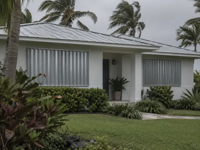 A coastal house with metal storm shutters fitted over the windows